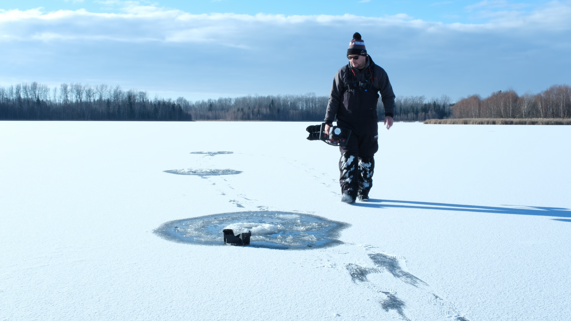 person walking on frozen lake drilling holes for ice fishing